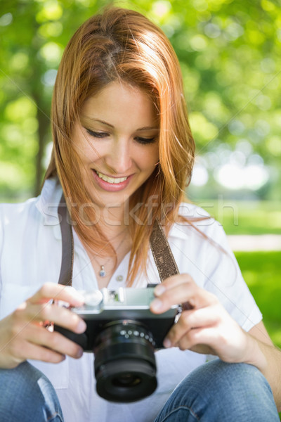 Stock photo: Pretty redhead looking at her camera in the park