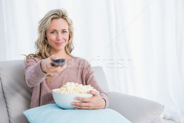 Smiling blonde changing tv channel while eating popcorn Stock photo © wavebreak_media