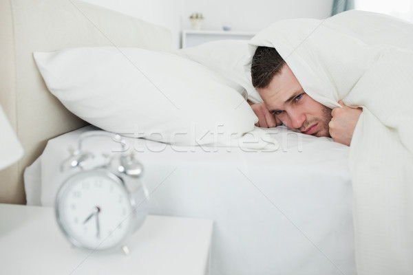 Stock photo: Annoyed man being awakened by an alarm clock in his bedroom