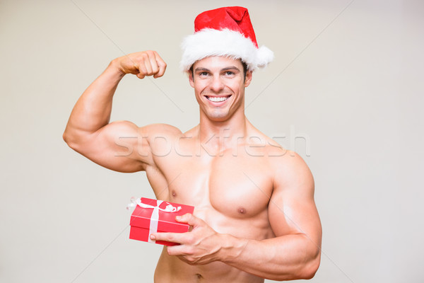 Portrait of shirtless macho man in santa hat holding gift Stock photo © wavebreak_media