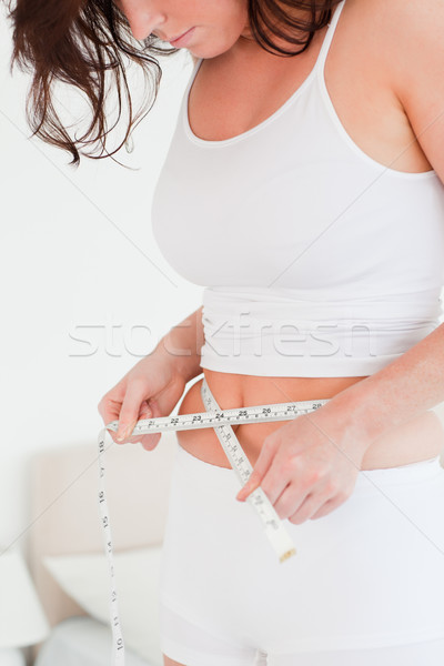 Charming brunette woman measuring her belly with a tape measure while standing in her bedroom Stock photo © wavebreak_media