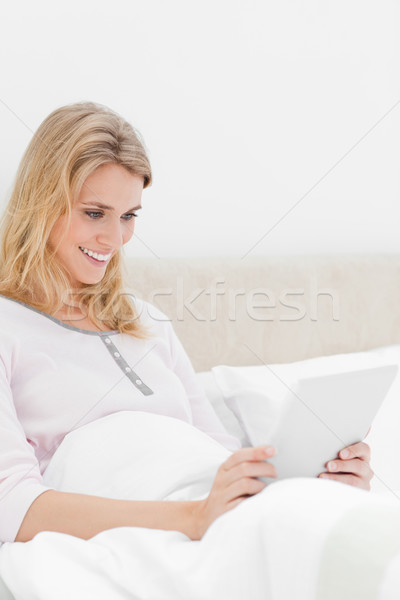 A woman sitting upright in the bed, with a tablet pc in her hands,watching the screen and smiling. Stock photo © wavebreak_media