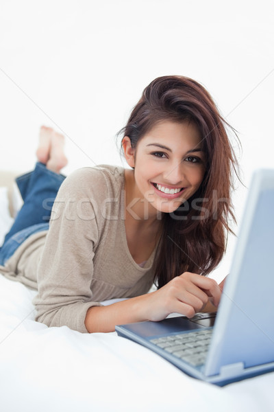 A smiling woman with her feet crossed, lying on the bed in front of her laptop. Stock photo © wavebreak_media