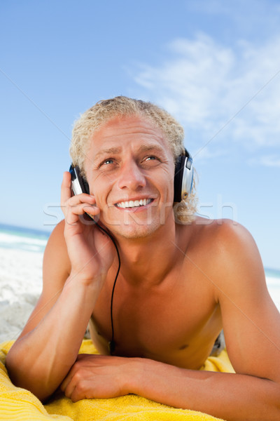 Foto stock: Sonriendo · hombre · playa · escuchar · música · toalla · de · playa · auricular