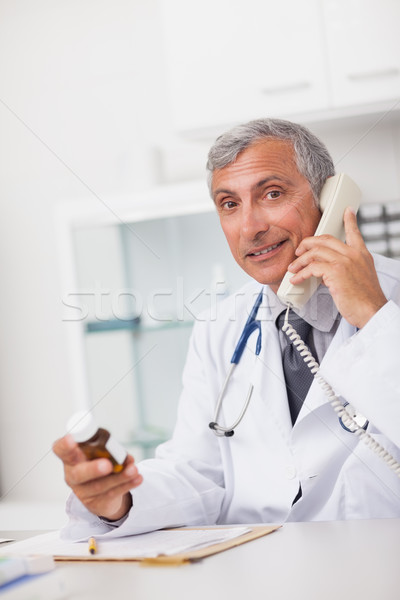 Doctor holding a drug box and a phone while sitting in a medical office Stock photo © wavebreak_media