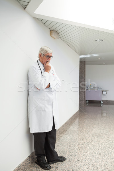Thinking doctor leaning against wall with had holding chin in hospital corridor Stock photo © wavebreak_media