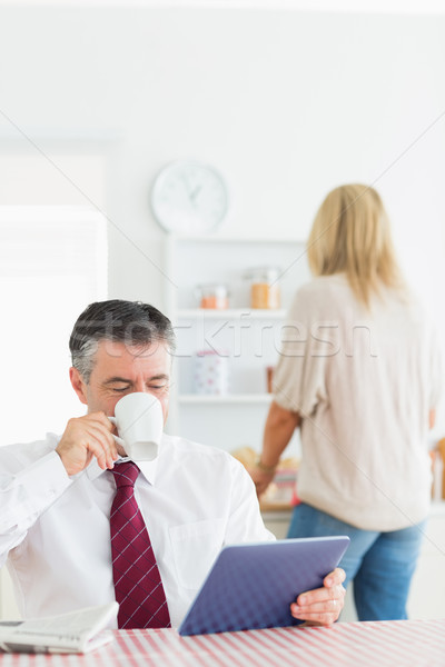 Stock photo: Man drinking coffee and using tablet pc in kitchen before work