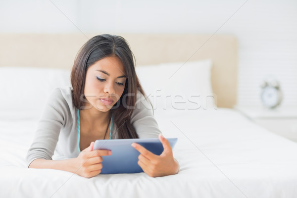 Stock photo: Young pretty girl lying on her bed using her tablet