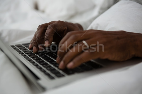 Stock photo: Cropped hands of man using laptop on bed
