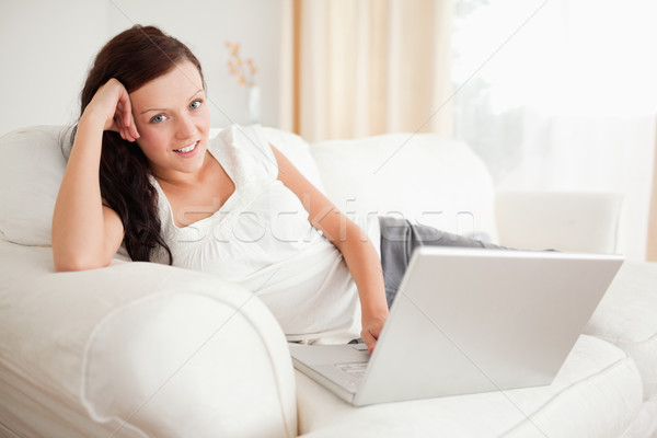 Stock photo: Red-haired woman relaxing on a sofa surfing the internet looking into the camera in the livingroom