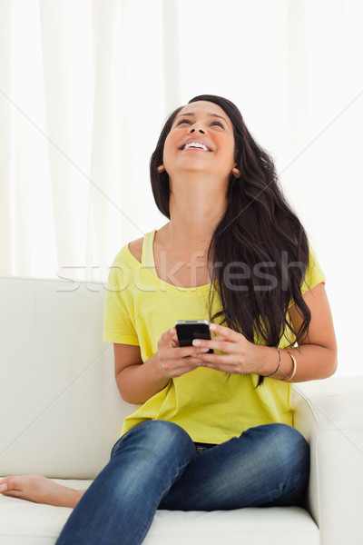 Happy Latino looking up while holding her cellphone being on a sofa Stock photo © wavebreak_media