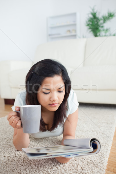 Stock photo: Woman holding a mug while reading a magazine on the floor in a living room