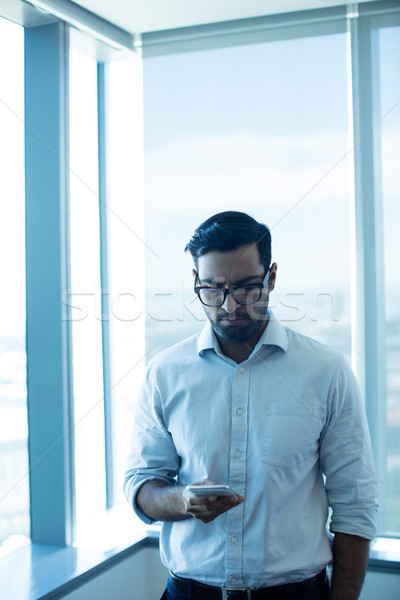 Young businessman using mobile phone while standing against glass window Stock photo © wavebreak_media