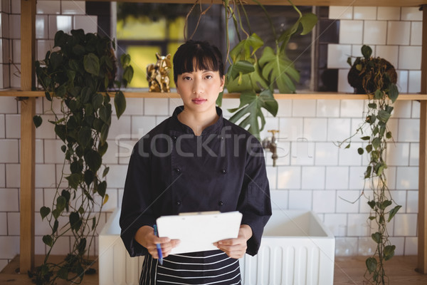 Portrait of young waitress holding clipboard against shelf Stock photo © wavebreak_media