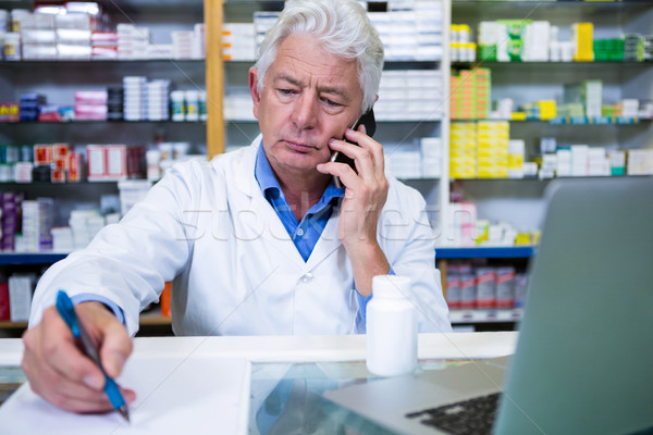 Pharmacist talking on mobile phone while writing prescriptions Stock photo © wavebreak_media