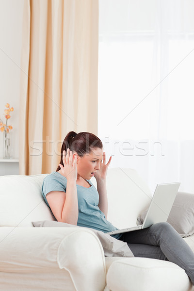Stock photo: Attractive upset woman gambling with her computer while sitting on a sofa in the living room
