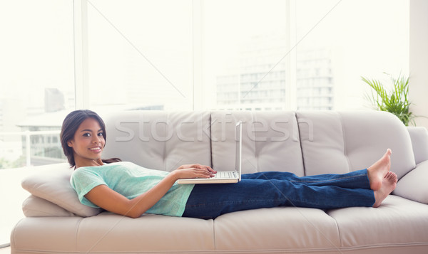 Young girl lying on sofa using her laptop smiling at camera Stock photo © wavebreak_media