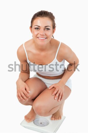 Portrait of a woman squatting on scales with the thumb up against a white background Stock photo © wavebreak_media