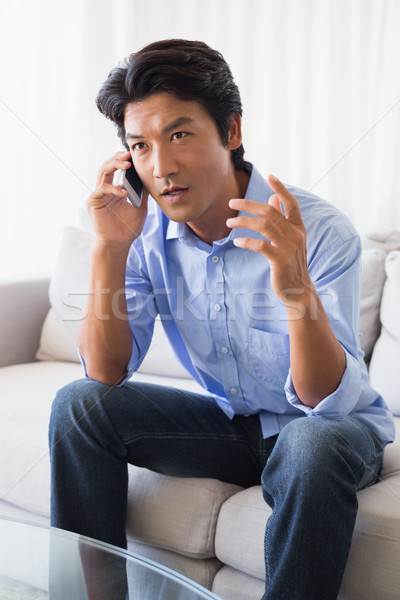 Stock photo: Annoyed man sitting on couch talking on phone