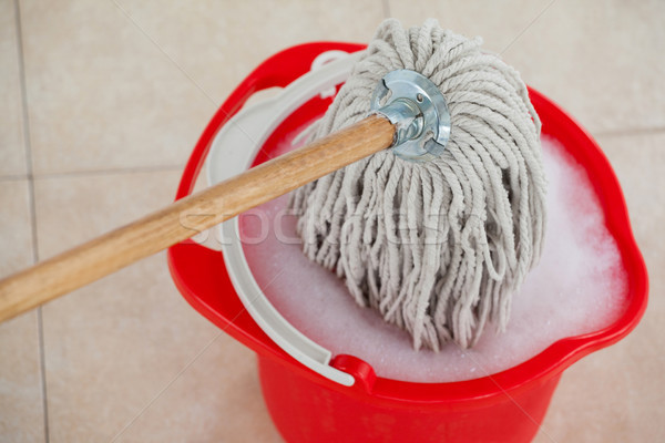 Stock photo: Bucket with foamy water and mopping the tile floor