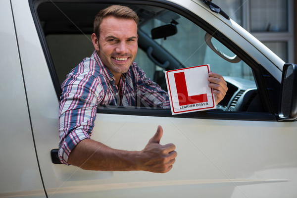 Young man gesturing thumbs up holding a learner driver sign Stock photo © wavebreak_media