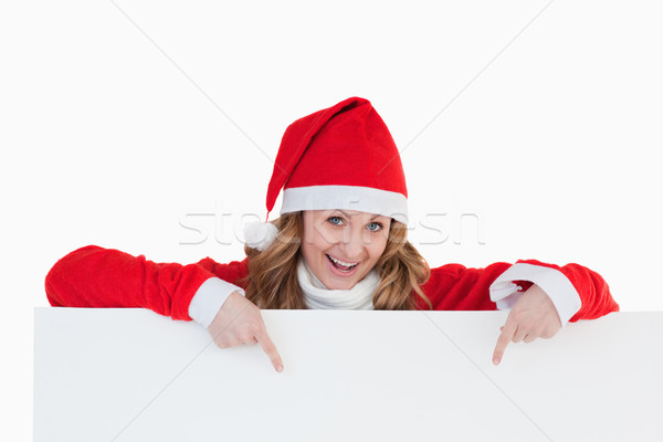 Stock photo: Attractive blond-haired woman dressed as Santa Claus holding a white board while showing something
