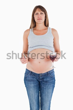 Stock photo: Beautiful pregnant woman holding a glass of red wine while standing against a white background