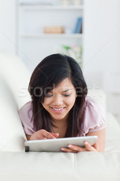 Stock photo: Smiling woman resting on a couch while playing with a tablet in a living room