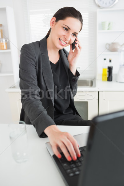 Stock photo: Smiling woman calling while using a laptop in a living room