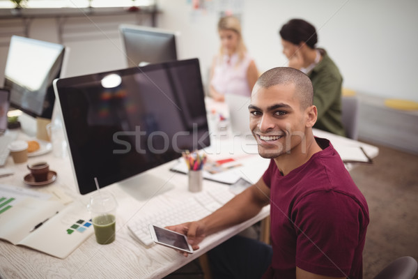 High angle portrait of smiling businessman holding mobile phone at office desk Stock photo © wavebreak_media