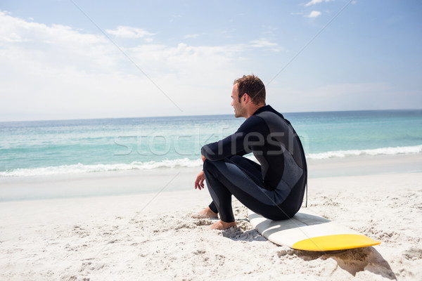 Happy surfer in wetsuit sitting with surfboard on the beach Stock photo © wavebreak_media