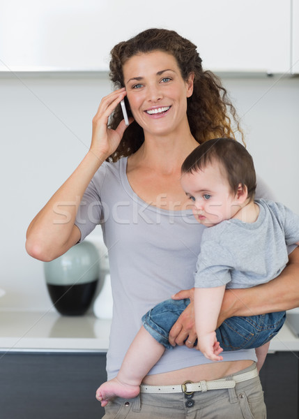 Happy woman answering smartphone while carrying baby Stock photo © wavebreak_media