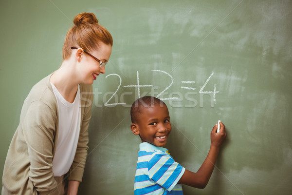 Teacher assisting boy to write on blackboard in classroom Stock photo © wavebreak_media