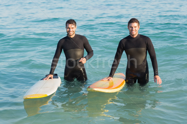 Two men in wetsuits with a surfboard on a sunny day Stock photo © wavebreak_media