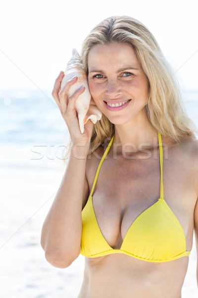 Smiling pretty blonde listening the seashell and looking at camera  Stock photo © wavebreak_media