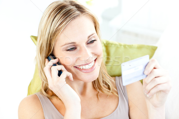 Charming young woman talking on phone holding a card in the living-room at home Stock photo © wavebreak_media