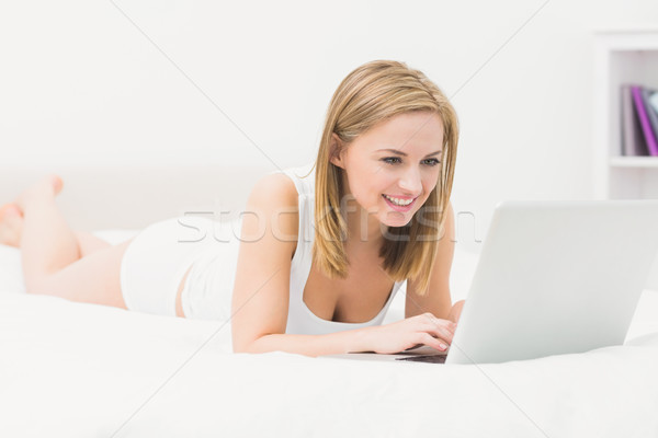 Beautiful happy woman lying in bed and using laptop Stock photo © wavebreak_media