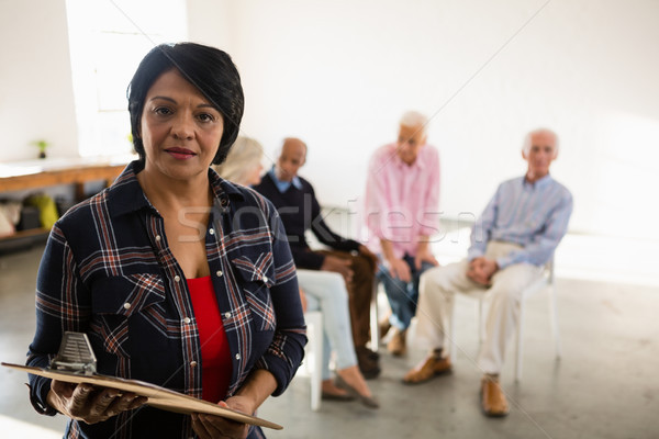 Portrait of senior woman holding clipboard with friends sitting in background Stock photo © wavebreak_media