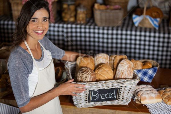 Stock photo: Female staff holding wicker basket of various breads at counter in bakery shop