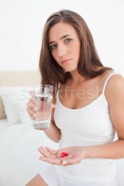 A woman is looking worried as she is deciding about taking the pills with a glass of water in her ot Stock photo © wavebreak_media