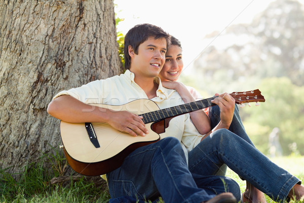 Stock photo: Man and his friend look into the distance as they listen to him playing the guitar while sitting aga