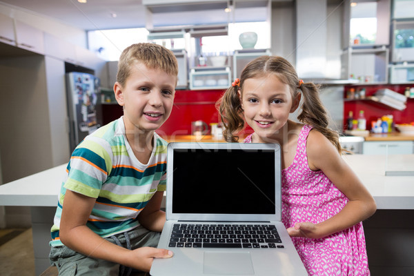 Stock photo: Smiling siblings holding laptop in kitchen