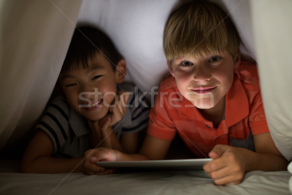 Portrait of siblings under bed sheet using digital tablet on bed Stock photo © wavebreak_media