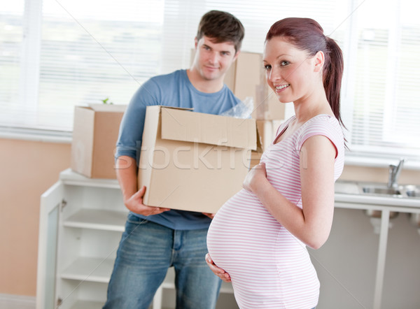 smiling future mother in new kitchen with husband in the background holding cardboard during removal Stock photo © wavebreak_media
