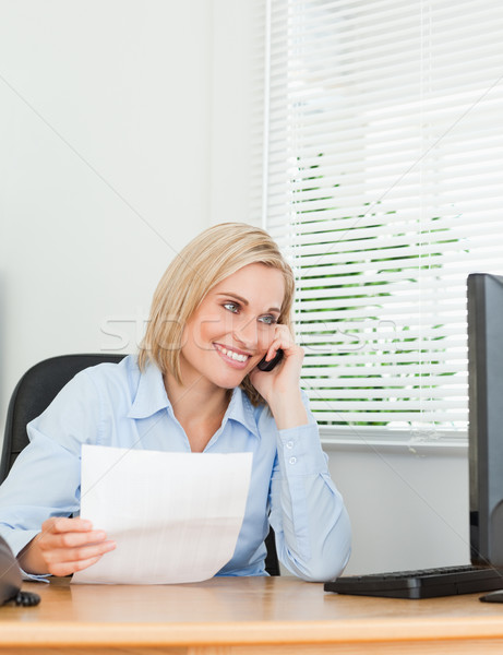 Businesswoman smiling at screen while phoning and holding a paper in her office Stock photo © wavebreak_media
