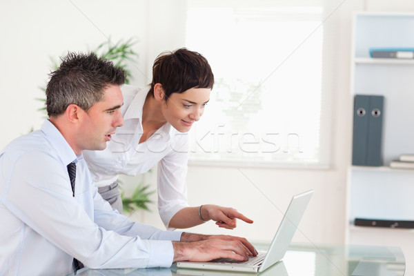 Stock photo: Woman pointing at something to her colleague on a laptop in an office