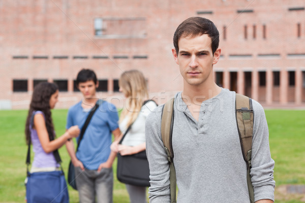 Stock photo: Lonely male student posing while his classmates are talking outside a building