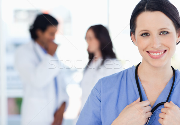 Young smiling nurse standing upright accompanied by her team who is standing behind her Stock photo © wavebreak_media
