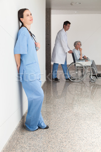 Nurse leaning against wall with doctor pushing patient in wheelchair Stock photo © wavebreak_media