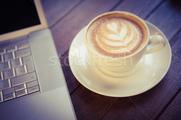 Cup of cappuccino with coffee art next to laptop Stock photo © wavebreak_media